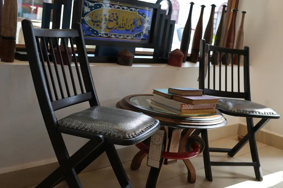 View of two vintage wooden chairs and a small round table stacked with books in a heritage interior.