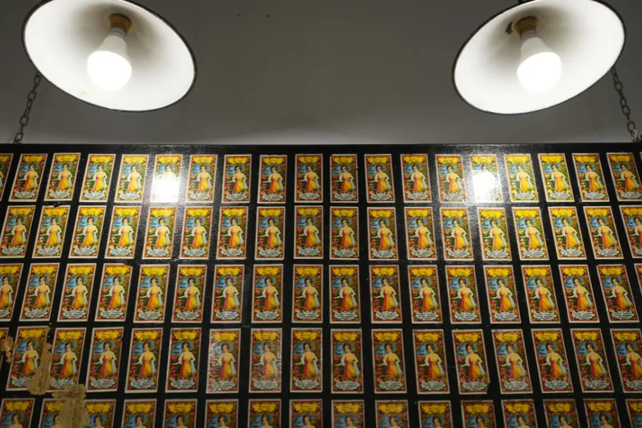 View of a patterned art wall with repeated traditional artwork displayed under warm ceiling lights.
