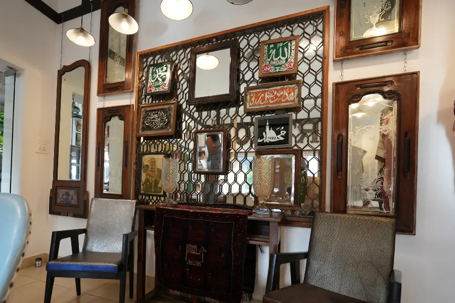 View of a decorative wall with vintage mirrors, framed calligraphy, and traditional wooden furniture.